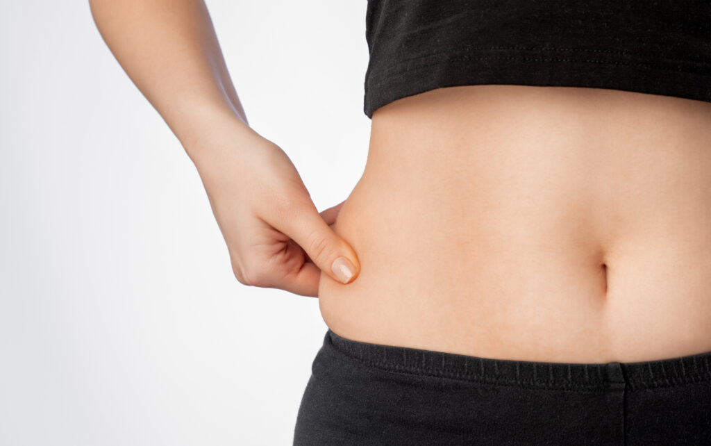 Girl pulls the skin on the abdomen, showing the body fat. Treatment and disposal of excess weight, the deposition of subcutaneous fat.